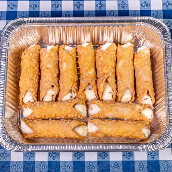 A foil tray filled with a dozen cannolis, featuring crispy shells and creamy white filling, on a blue and white checkered tablecloth.