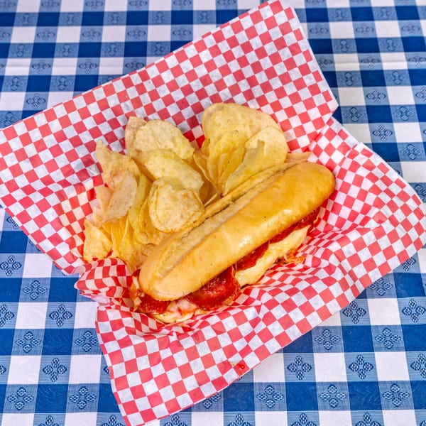 Big Dog's Pizza pepperoni sub with melted cheese and potato chips in a red and white checkered basket.