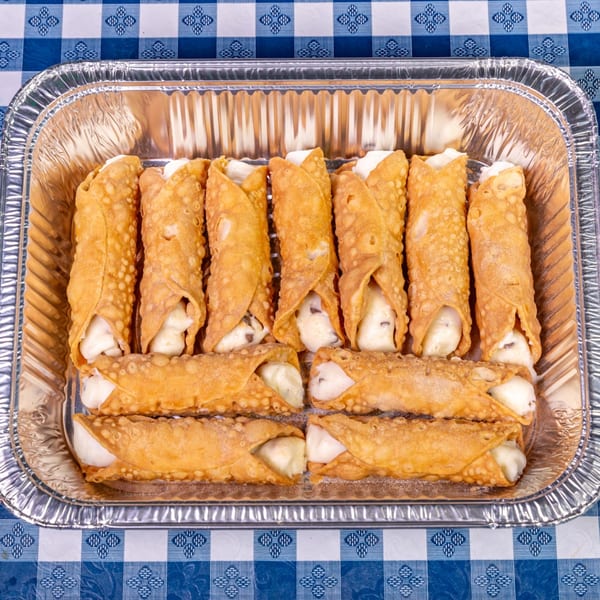 A foil tray filled with golden-brown cannolis, featuring creamy white filling, on a blue and white checkered tablecloth.