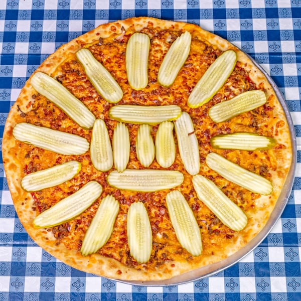 A Big Dog's Pizza with ground beef and pickle slices arranged in a circular pattern on a blue checkered tablecloth.